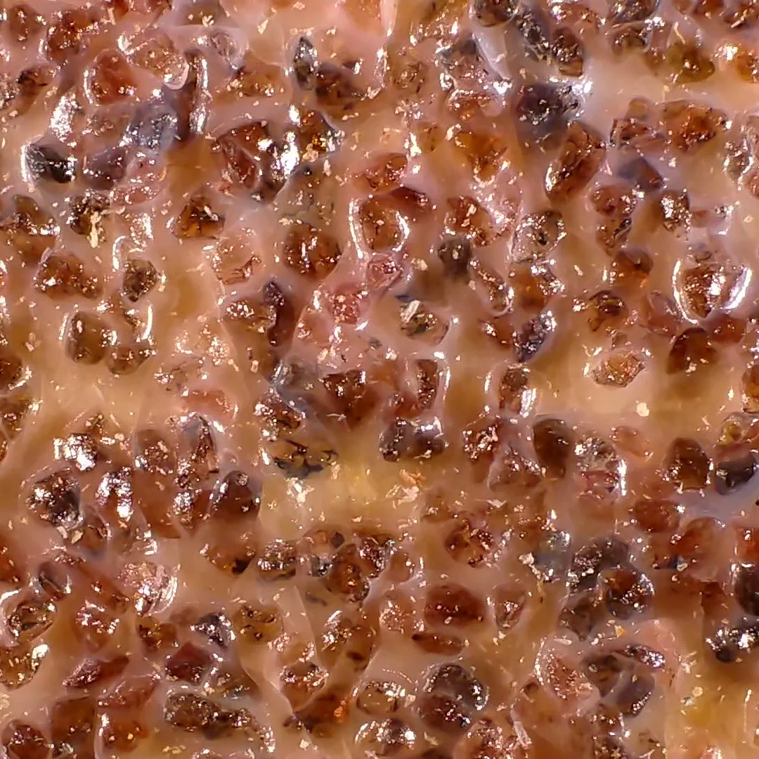 Magnified view of 60 grit aluminum oxide sandpaper, showing brownish crysals over a glued backing